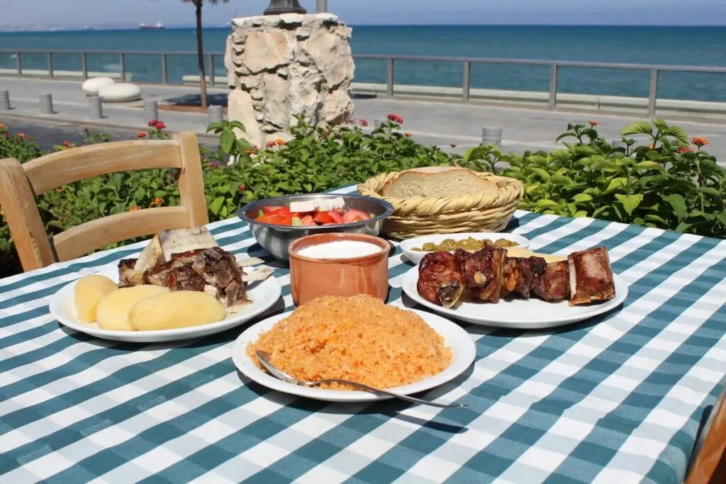 a table at seaside militzis restaurant in larnaca cyprus with a blue and white tablecloth and plates with bread rice lamb and potatoes