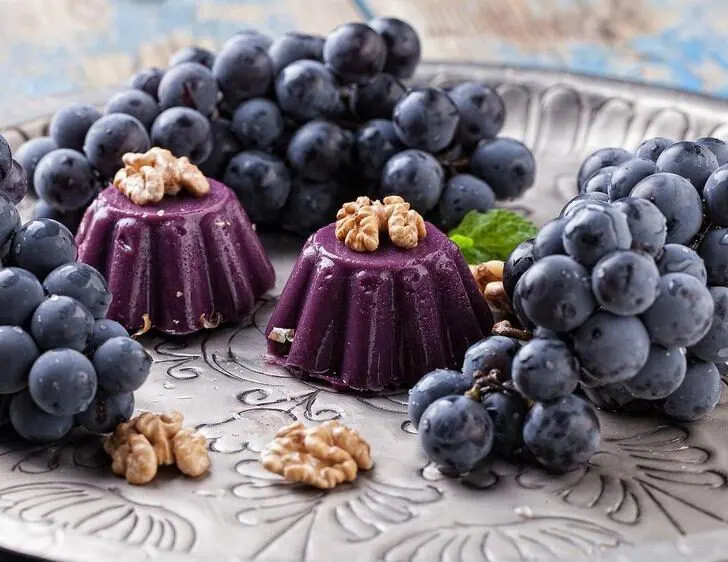 a plate of red grapes with two pelamushi georgian desserts in the center