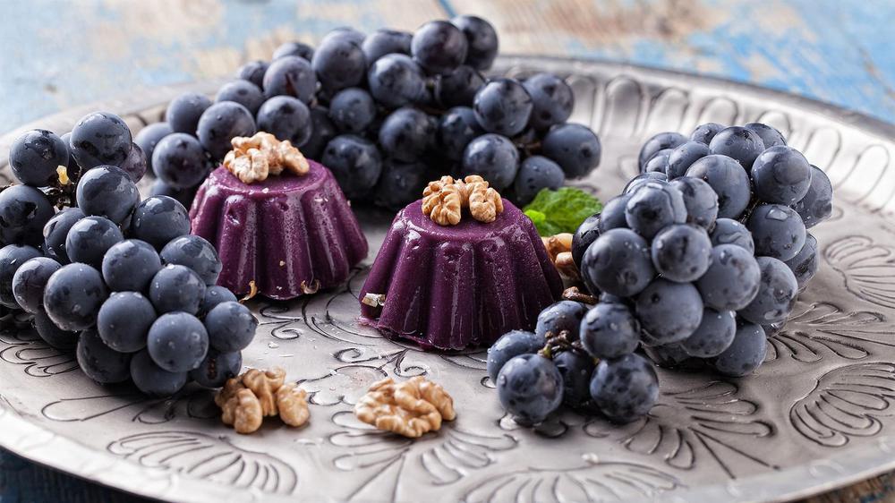 a plate of red grapes with two pelamushi georgian desserts in the center