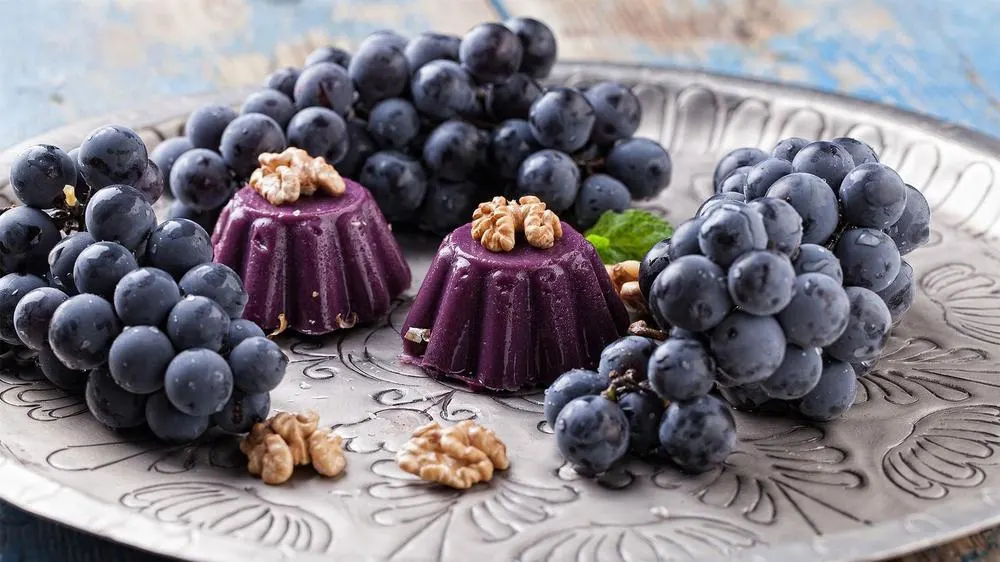 a plate of red grapes with two pelamushi georgian desserts in the center