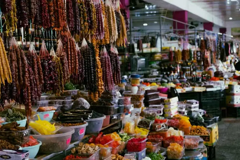 a street market stall at dezerter bazaar tbilisi georgia with fruit on a table and churchkhela dried nuts in grape juice hanging from above