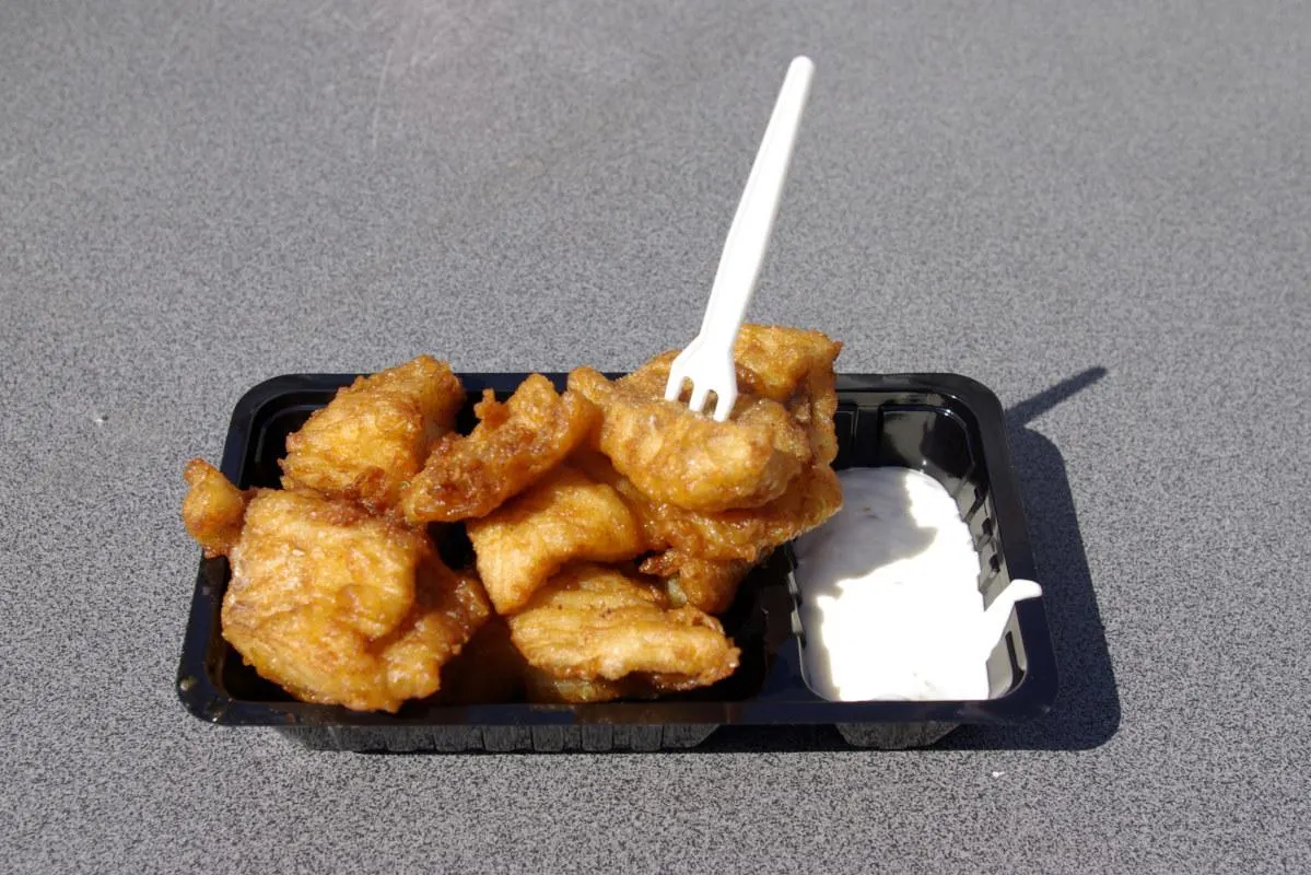 Kibbeling on a plastic plate with sauce and a fork