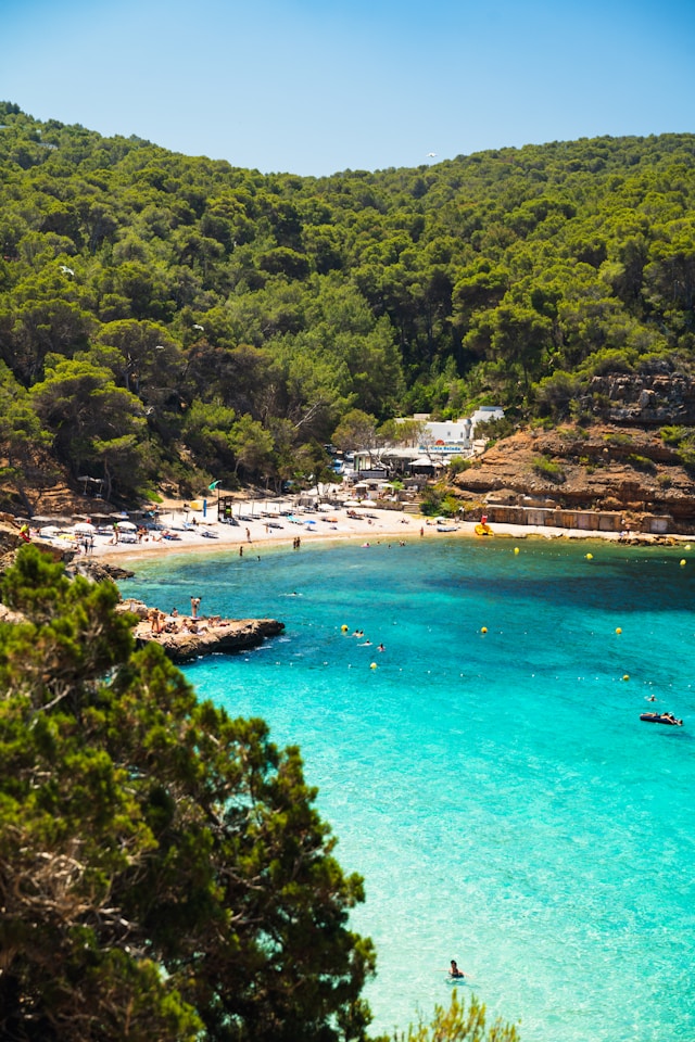 blue mediterranean sea and a white sandy beach with sunbeds and parasols in ibiza balearic islands spain