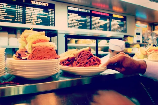 a pastrami sandwich on rye bread on a white plate being served from a deli counter in new york city usa