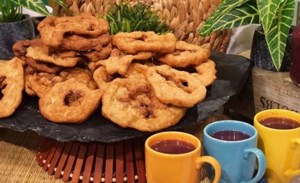 Bolivian buñuelos on a plate with mugs of api next to it