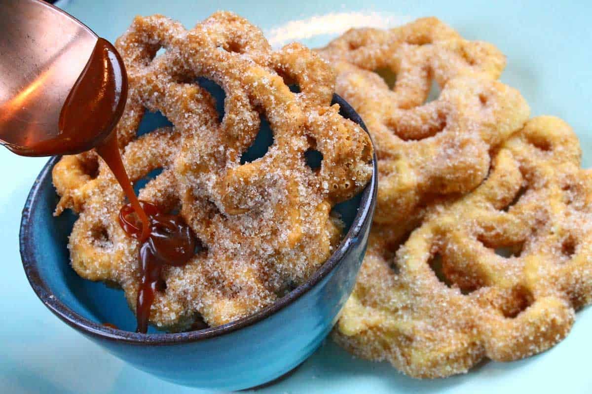 Bolivian buñuelos on a plate, covered in sugar and syrup