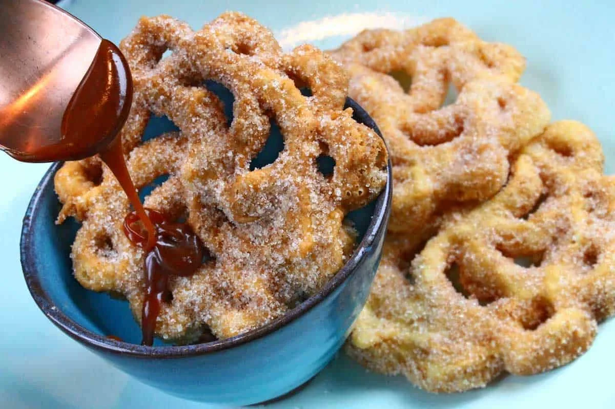Bolivian buñuelos on a plate, covered in sugar and syrup