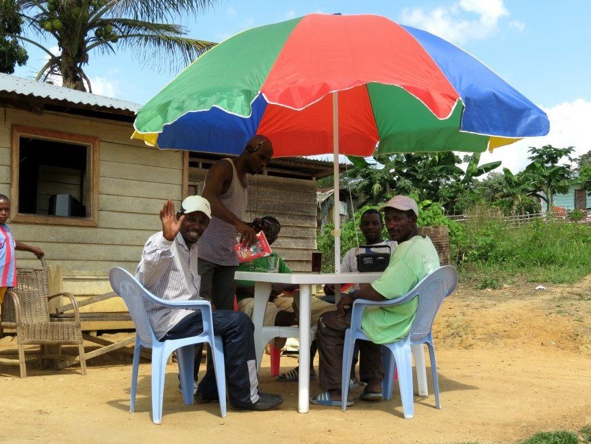 People sitting at a small table under an umbrella, in front of a house in Equatorial Guinea