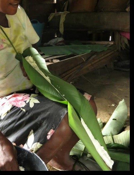 A woman preparing a roll of fermented cassava inside a banana leaf