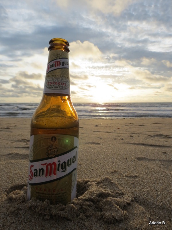 A bottle of San Miguel beer on the beach at sunset
