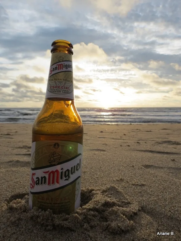 A bottle of San Miguel beer on the beach at sunset