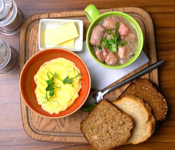 a green cup filled with dublin coddle served with bread and potatoes on a wooden board at the doxty house restaurant in dublin ireland