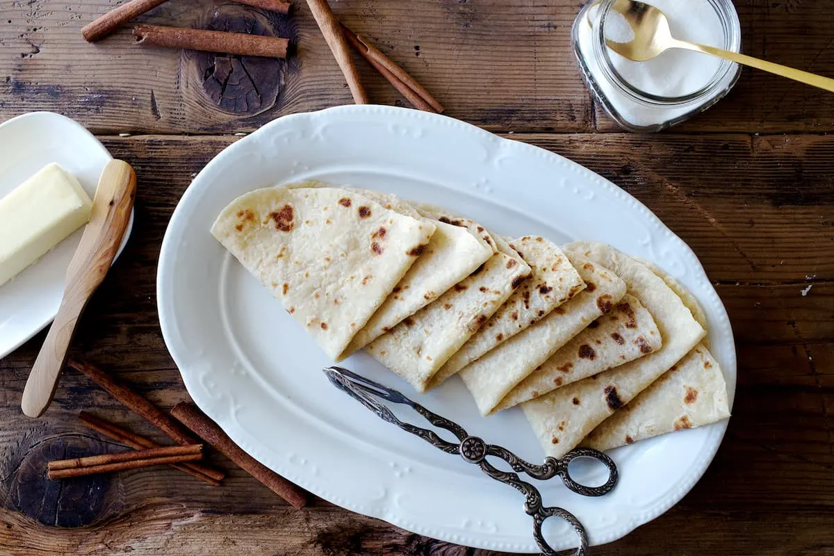 norwegian flatbread lefse served in triangles on a white plate with a pair of scissors on the side