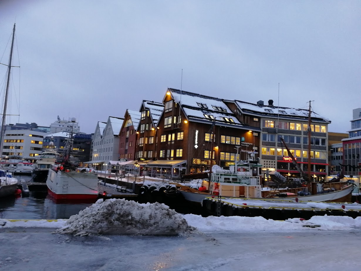 a wooden building next to a harbour with boats on a snowy day in tromso norway