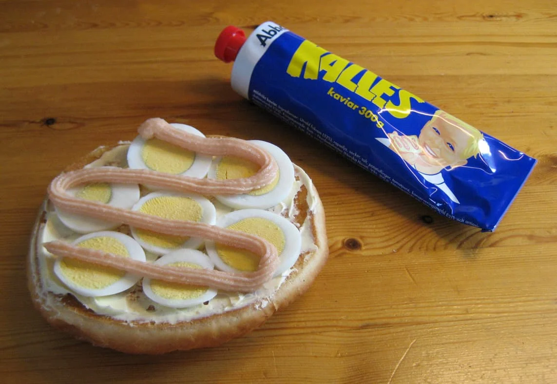 an aluminium tube containing kalles kaviar a swedish fish roe spread next to a bread roll with sliced boiled eggs