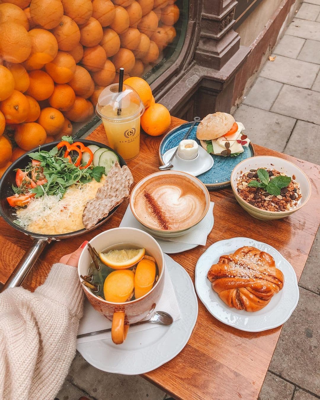 a table outside cafe schweizer in stockholm sweden with a cup of coffee and plates containing scrambled eggs, pastries and granola with yoghurt