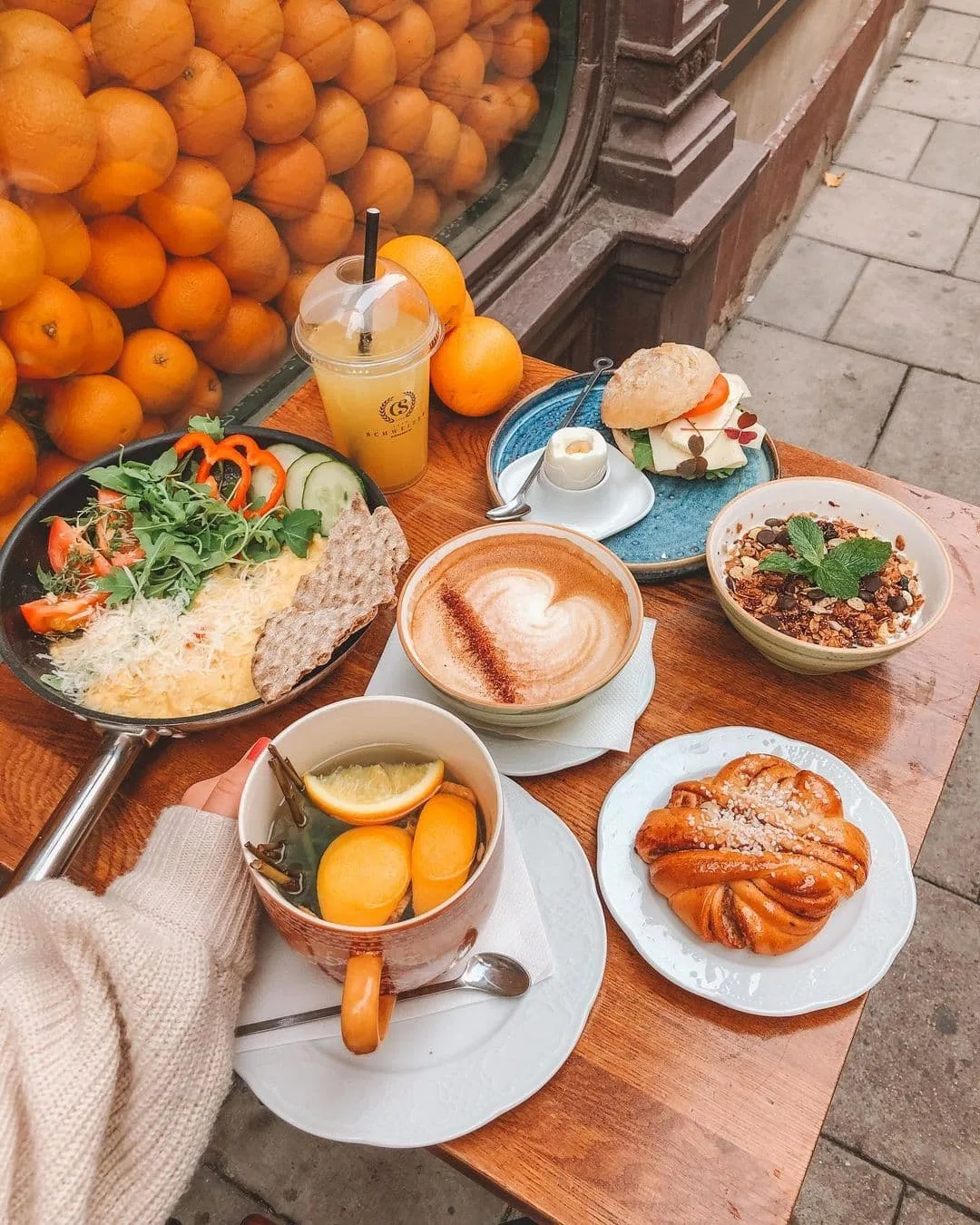 a table outside cafe schweizer in stockholm sweden with a cup of coffee and plates containing scrambled eggs, pastries and granola with yoghurt