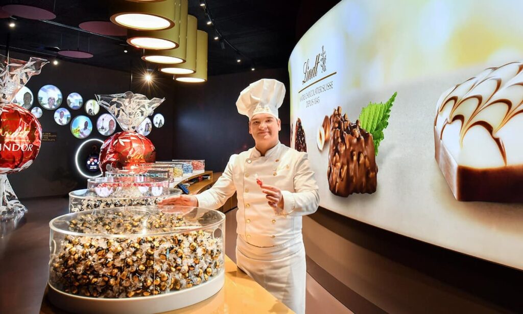 a chocolatier stands next to a display of lindt chocolate truffles at the home of chocolate in zurich switzerland