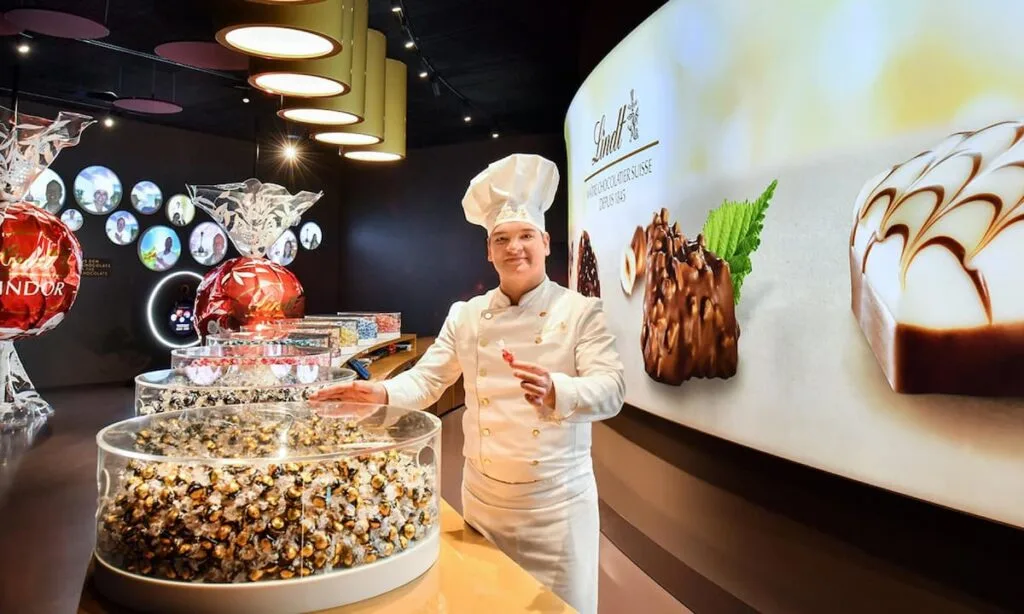 a chocolatier stands next to a display of lindt chocolate truffles at the home of chocolate in zurich switzerland