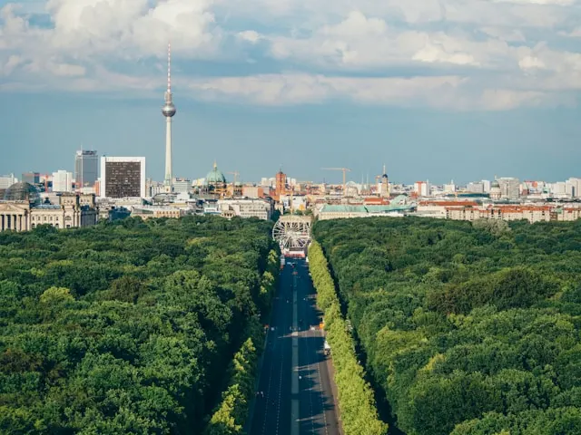 trees in tiergarten berlin germany separatrd by a road with a ferris wheel at the end and the fernsehturm in the background