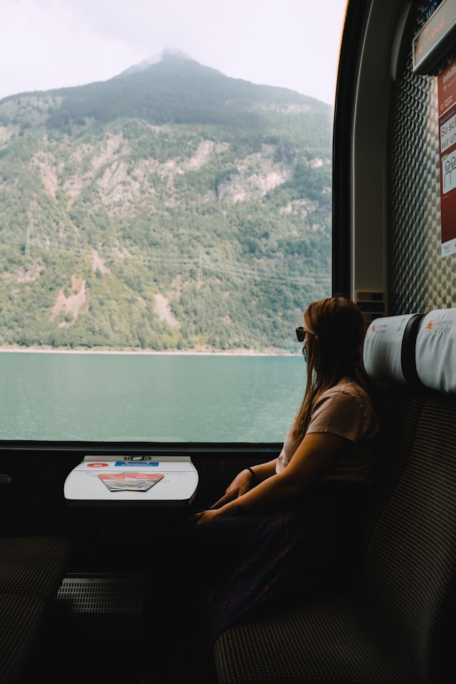 a woman looking at a mountain and lake from a seat with a table on the glacier express train in switzerland