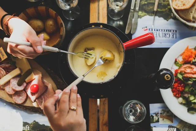 two people dip potatoes on forks in to a cheese fondue