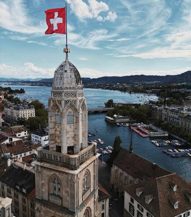 a clock tower with the swiss flag on top overlooking boats on lake zurich switzerland