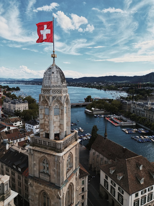 a clock tower with the swiss flag on top overlooking boats on lake zurich switzerland