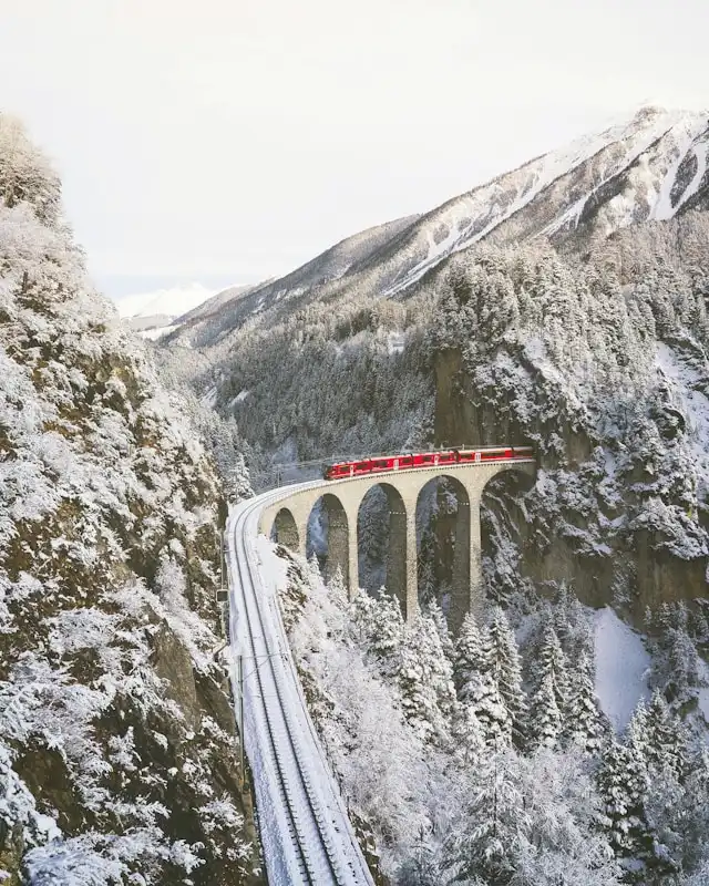 a red and white sbb train on a viaduct between snowy mountains in switzerland