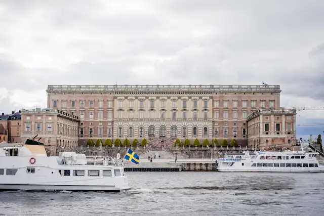 the royal palace backs on to the water where boats pass in gamla stan stockholm sweden