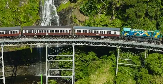 A view of Kuranda's traditional train in front of the jungle and a waterfall
