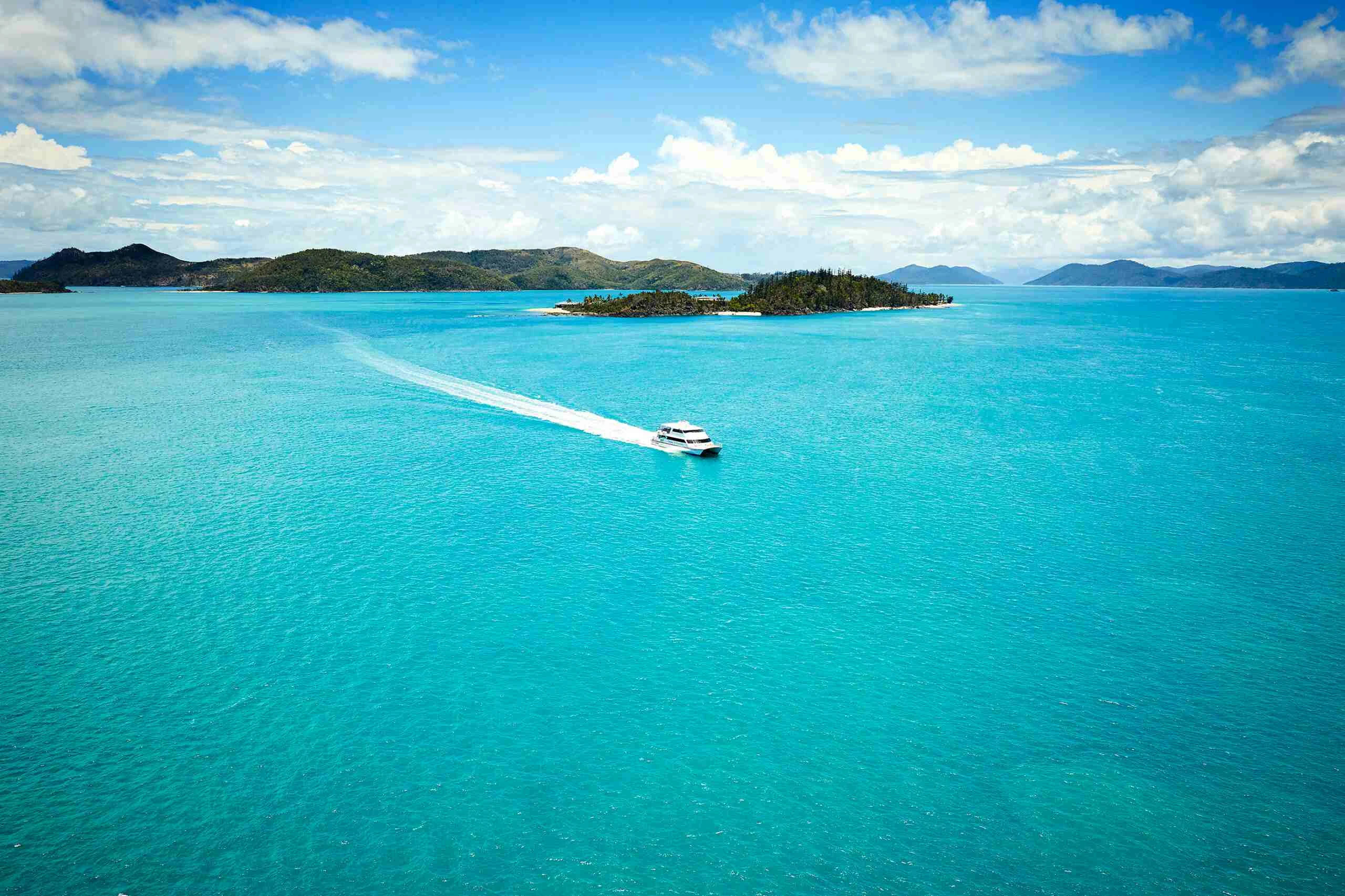 A turquoise sea with islands in the background and a boat running through the water