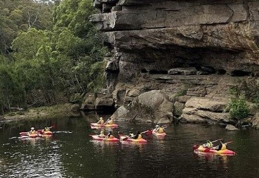 People canoeing on a river next to a rock face