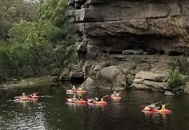 People canoeing on a river next to a rock face