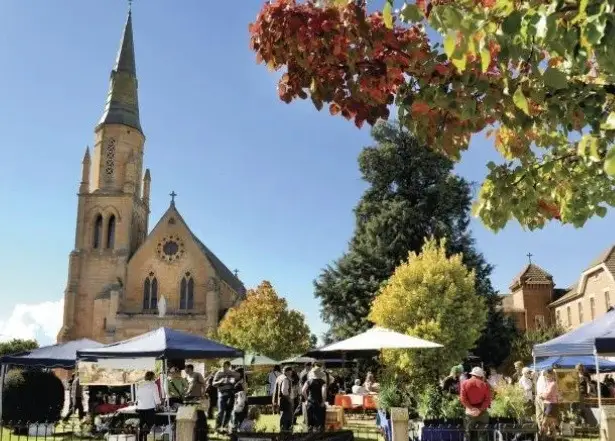 A market at Mudgee, next to a church, with people milling about