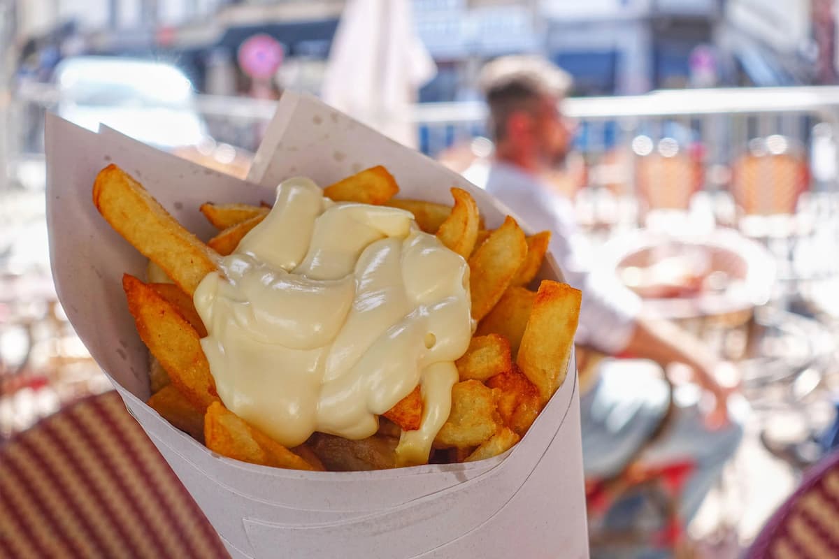 a white cone containing belgian frites topped with mayonnaise 
