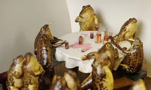 stuffed frogs sitting around a table with a white table cloth at froggyland museum in split croatia