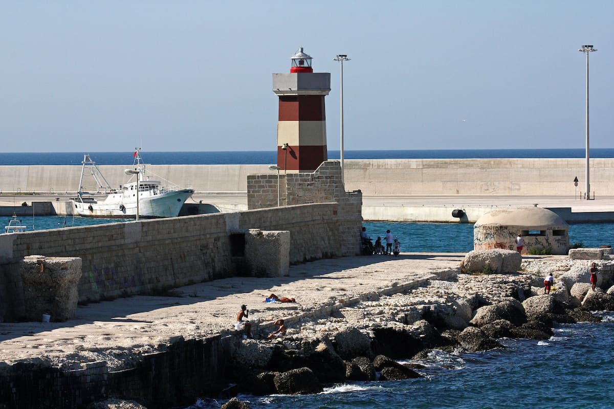a red and white striped lighthouse on a harbor wall in monopoli puglia italy
