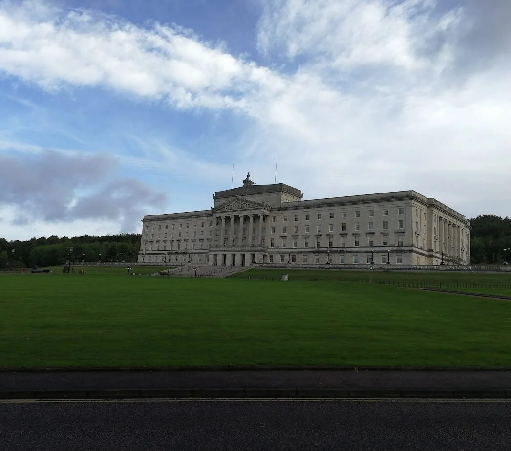 a large stone building with a grass expanse in front is stormont home of the northern ireland assembly in belfast