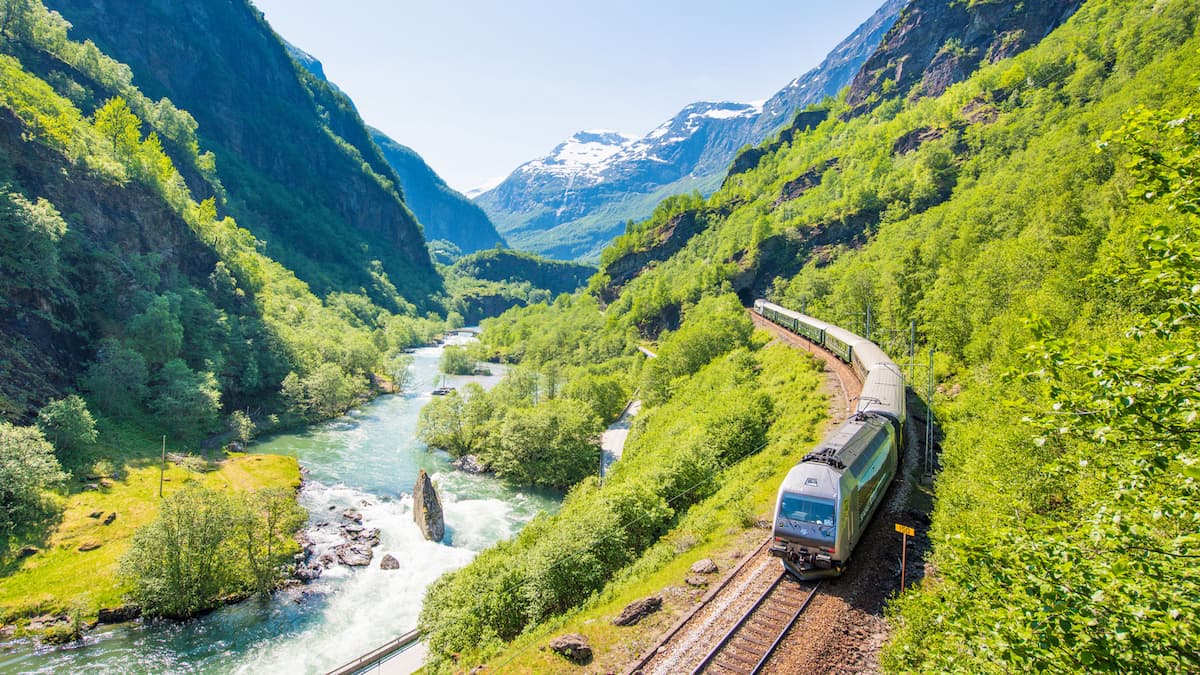 a green train beside a river on the flam railway in norway