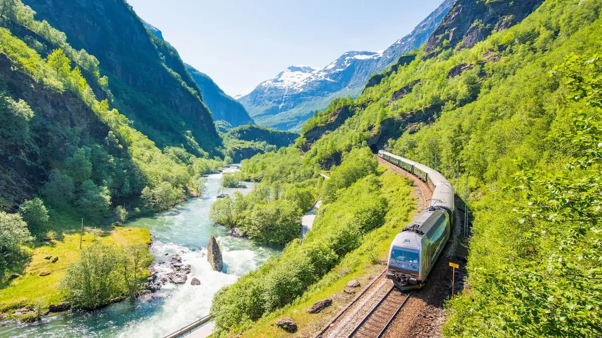 a green train beside a river on the flam railway in norway