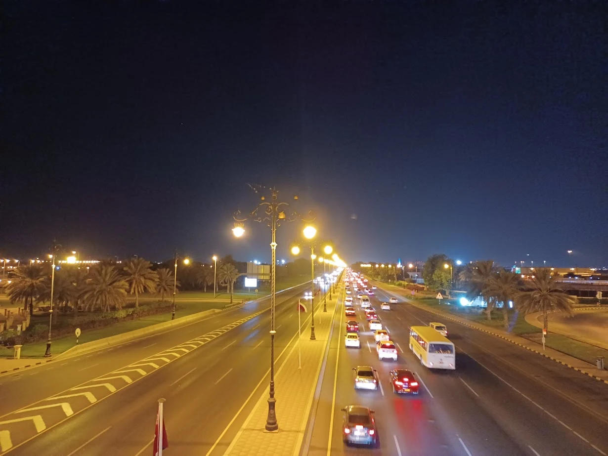 street lights illuminate a dark highway with cars and buses in muscat oman