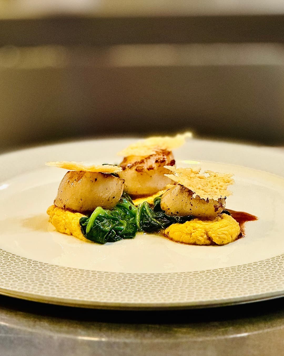 Seared scallops, pumpkin mousse, pecorino crisps, and sautéed spinach.
