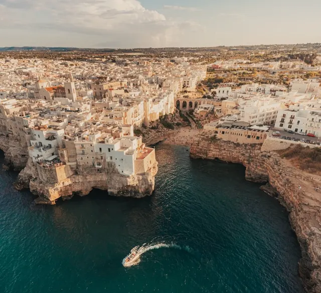 a boat on the adriatic sea with the whitewashed houses of polignano a mare puglia italy atop a cliff in the background