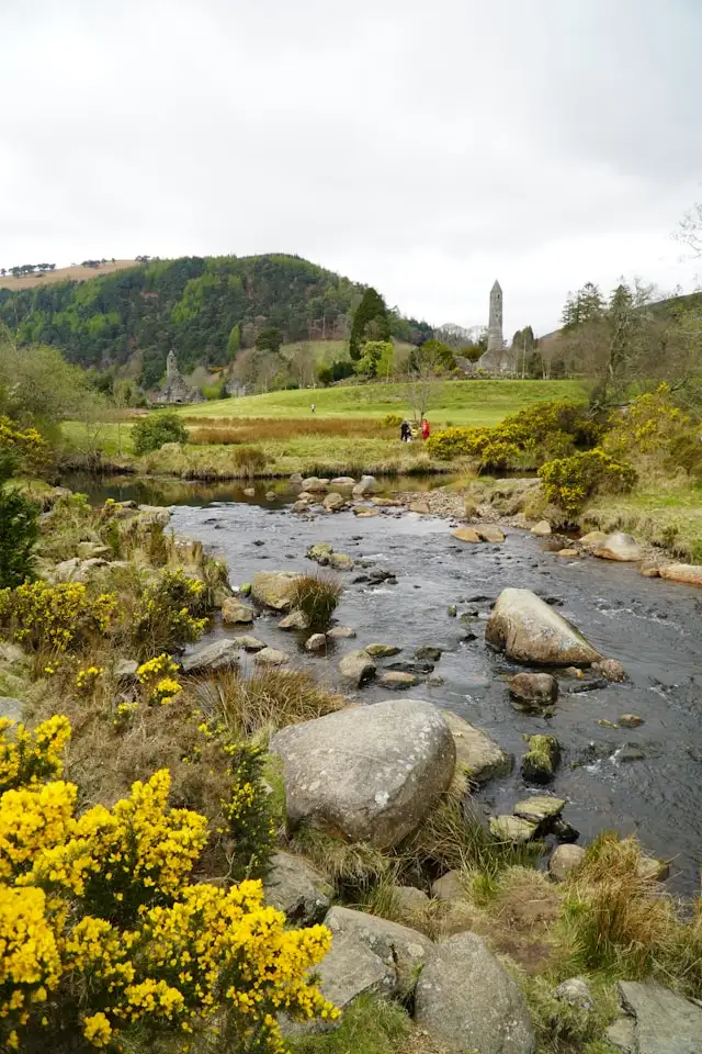 a river with stepping stones in front of a monument at glendalough monastic site in wicklow ireland