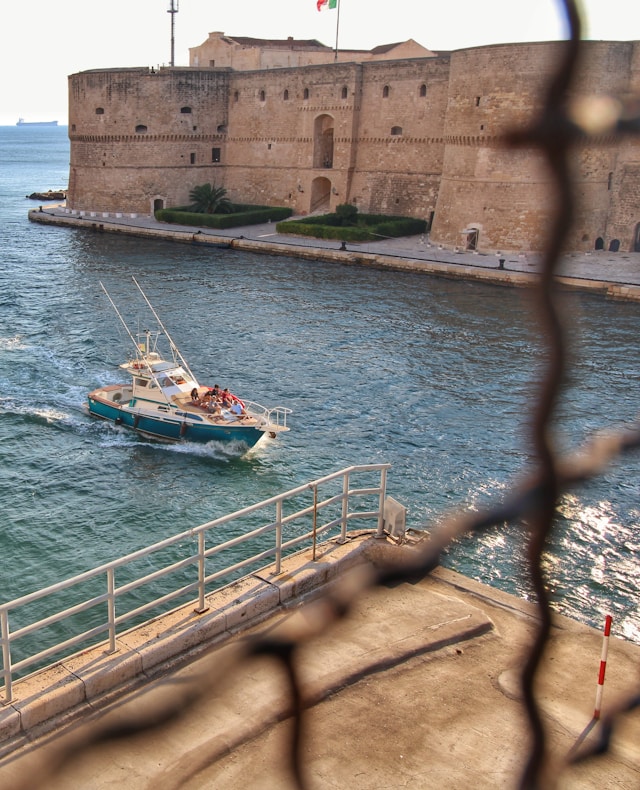 the 15th century aragonese castle in the background as a motorboat darts through the water in taranto puglia italy