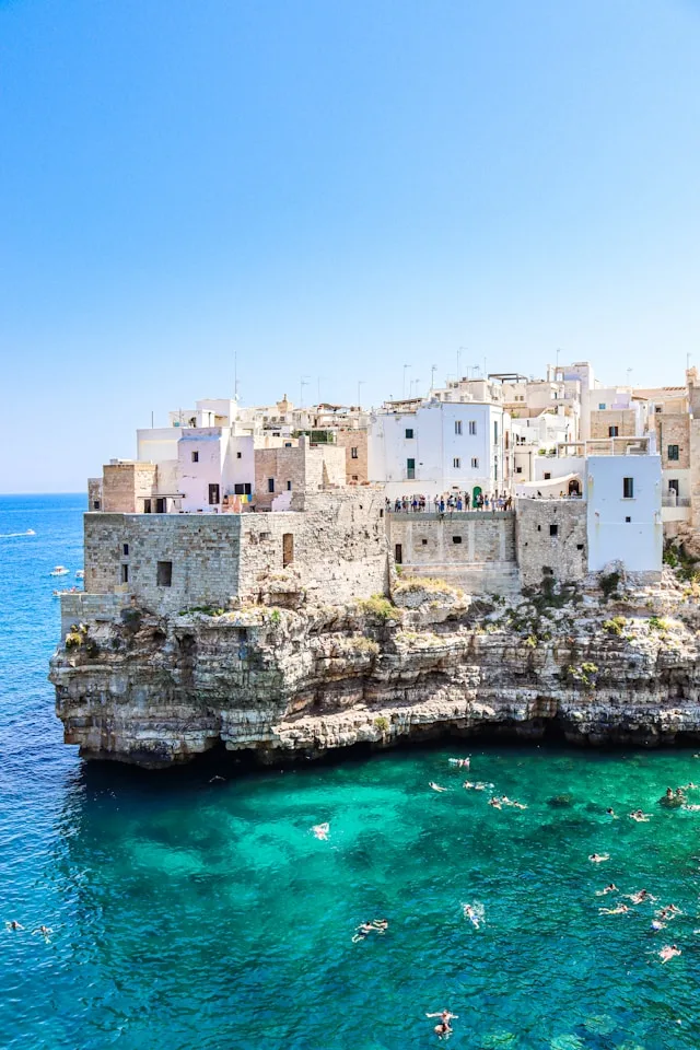 whitewashed houses behind a turquoise ocean in puglia itlay