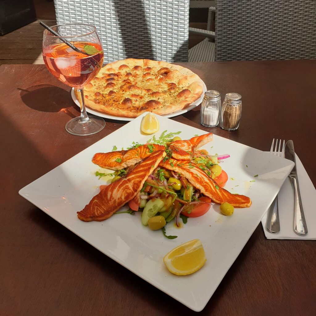 homemade garlic bread and a salmon salad on a white plate with an aperol spritz in the background at confetti's kosher italian restaurant in the jewish quarter antwerp belgium