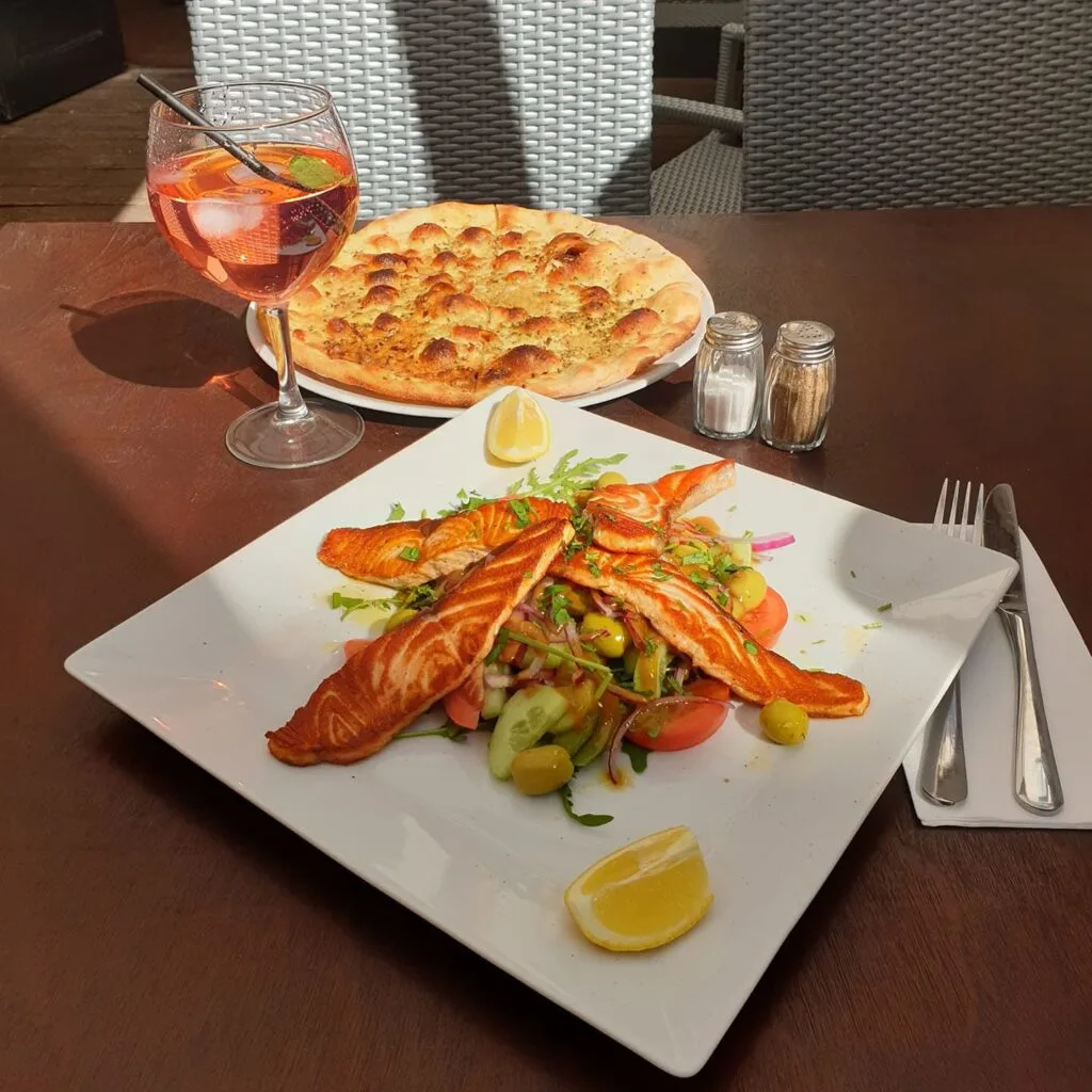 homemade garlic bread and a salmon salad on a white plate with an aperol spritz in the background at confetti's kosher italian restaurant in the jewish quarter antwerp belgium