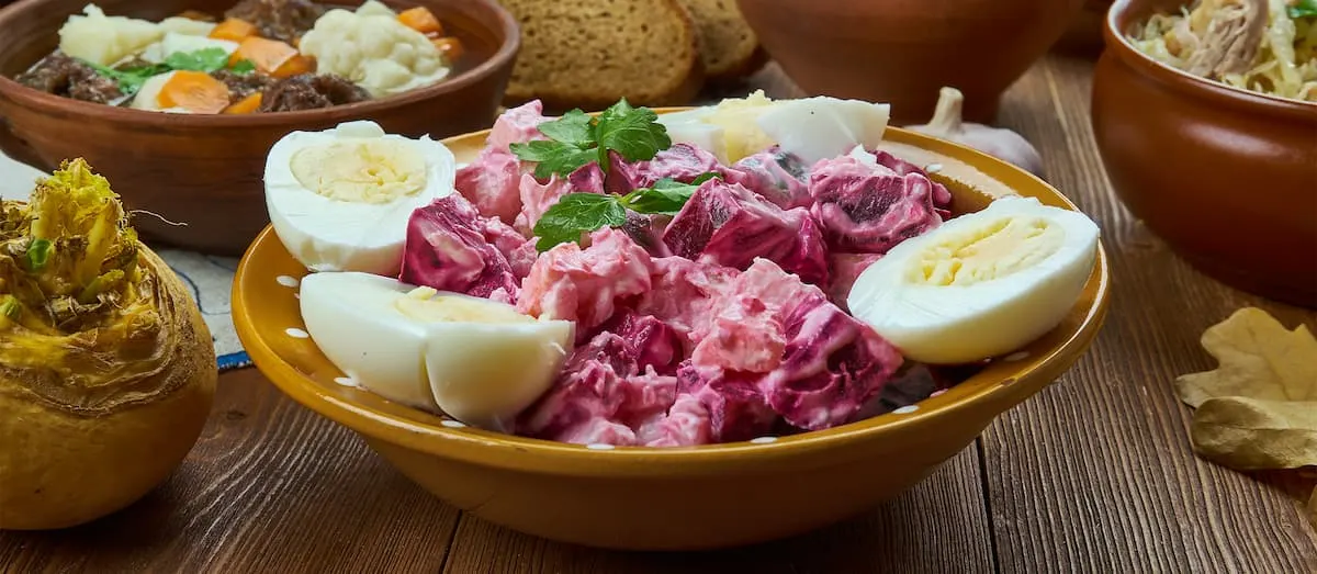a brown bowl containing potato salad mixed with beetroot and garnished with eggs known as rosolje in estonia